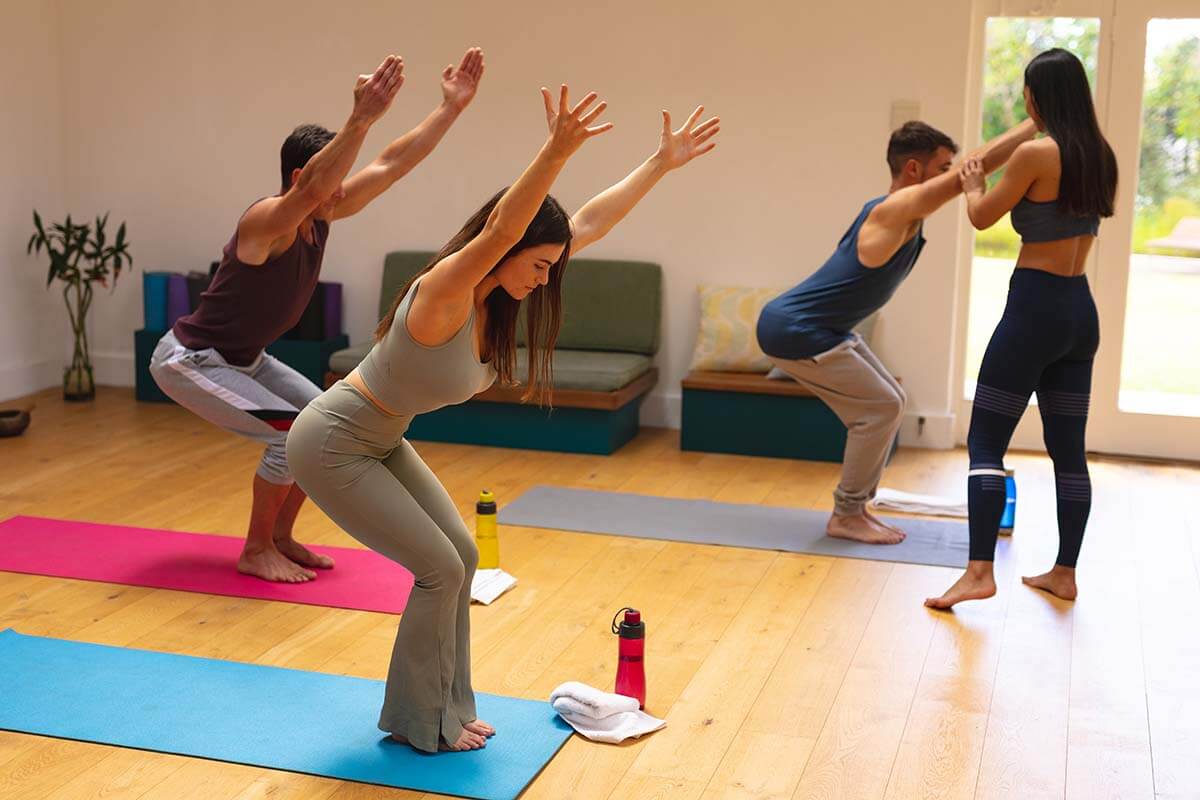 Three people doing yoga in a room with an instructor touching the arm of one of the people.