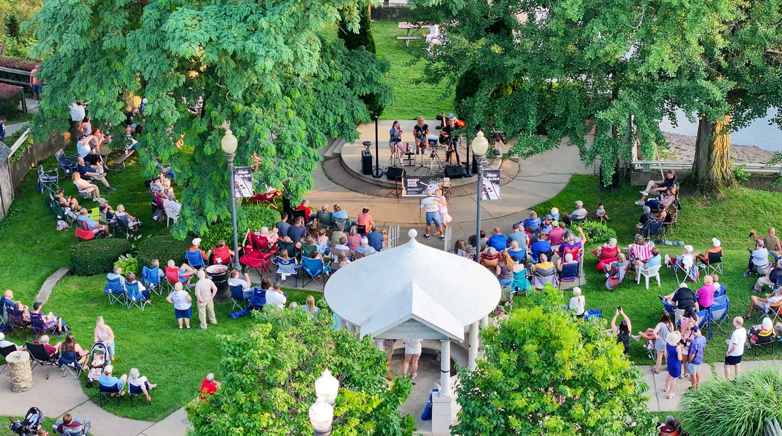 An aerial photo of a group of people on a green lawn watching a 3-piece band perform