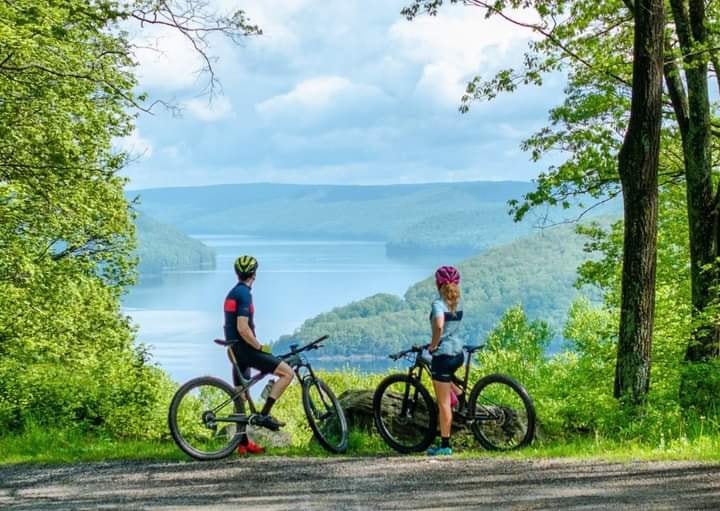 Two mountain bikers standing with their bikes looking out over the Allegheny Reservoir from a scenic overlook at Jakes Rocks in Warren County PA.